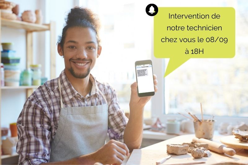 Agenda partagé avec le client : un homme dans sa cuisine recevant un SMS de notification de rendez-vous sur son mobile